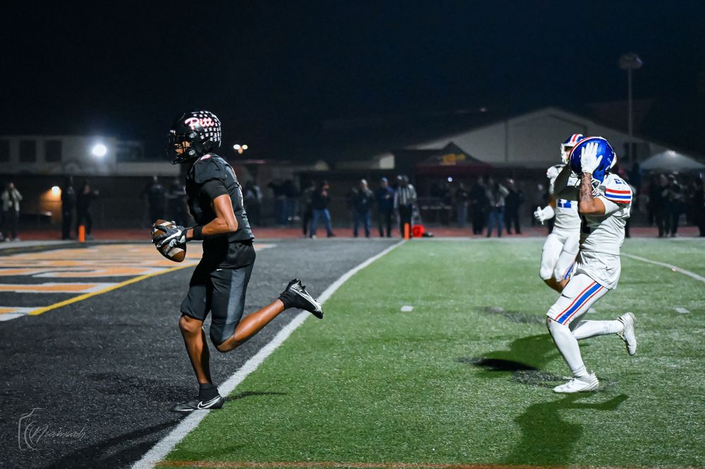 Football players in action during a night game with stadium lights illuminating the field.