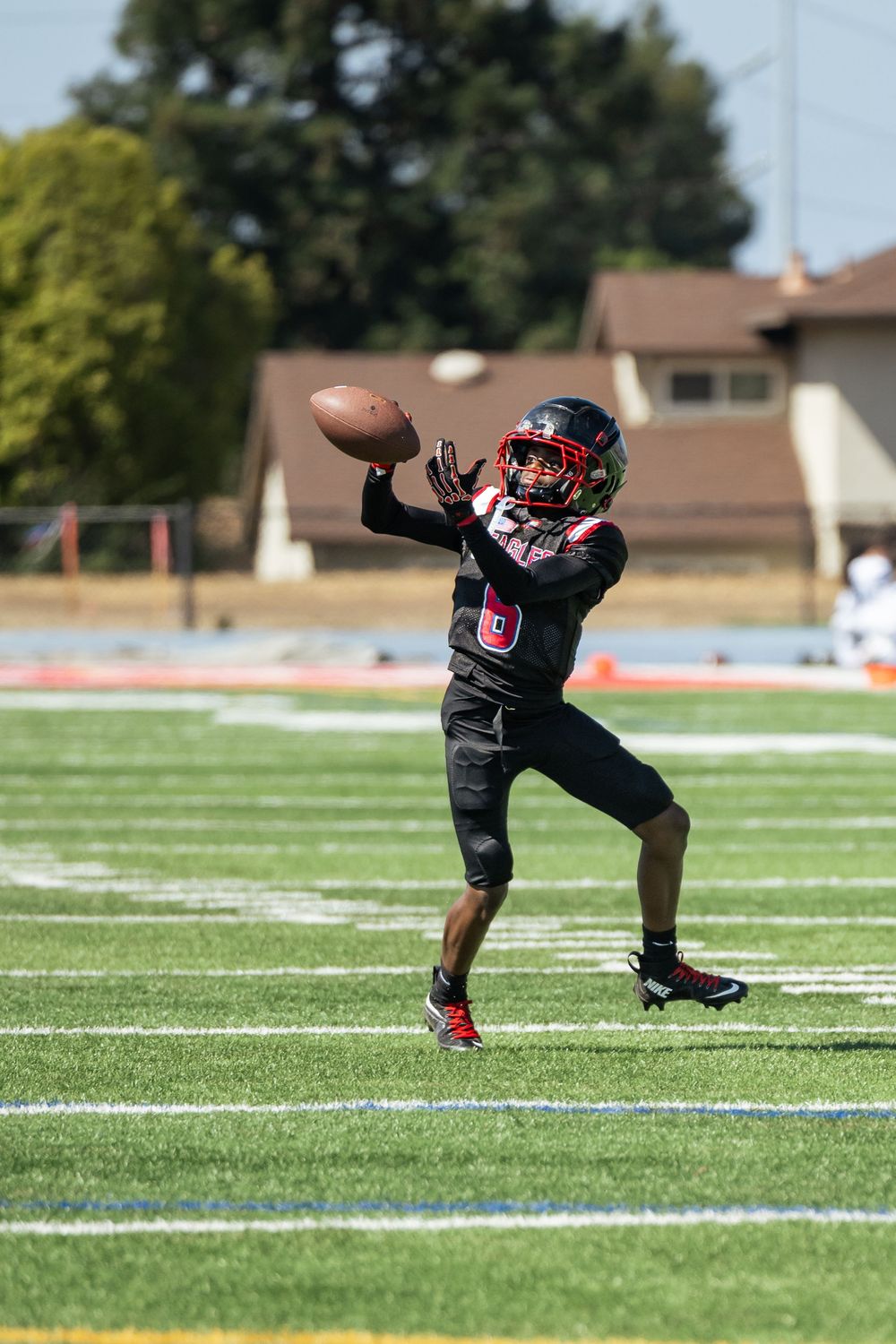 Football player in black uniform practices kicking drills on green turf field.
