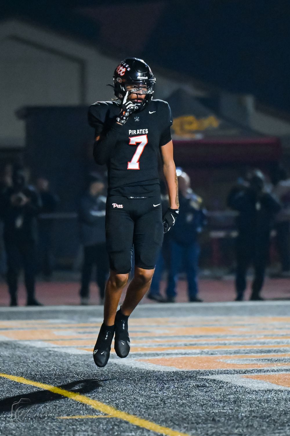 Football player in black Pirates uniform running on the field during nighttime game.