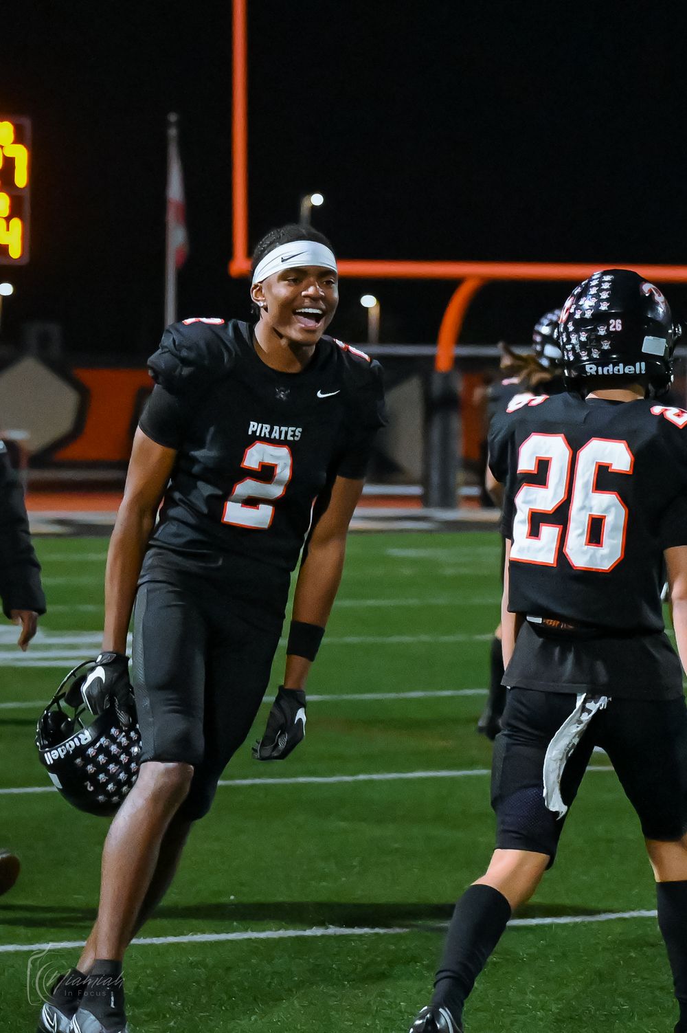 Football players in black Pirates uniforms line up on the field during a night game.