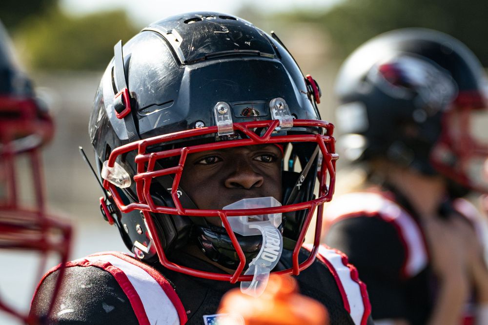 Close-up of football helmets with red facemasks on the sideline.