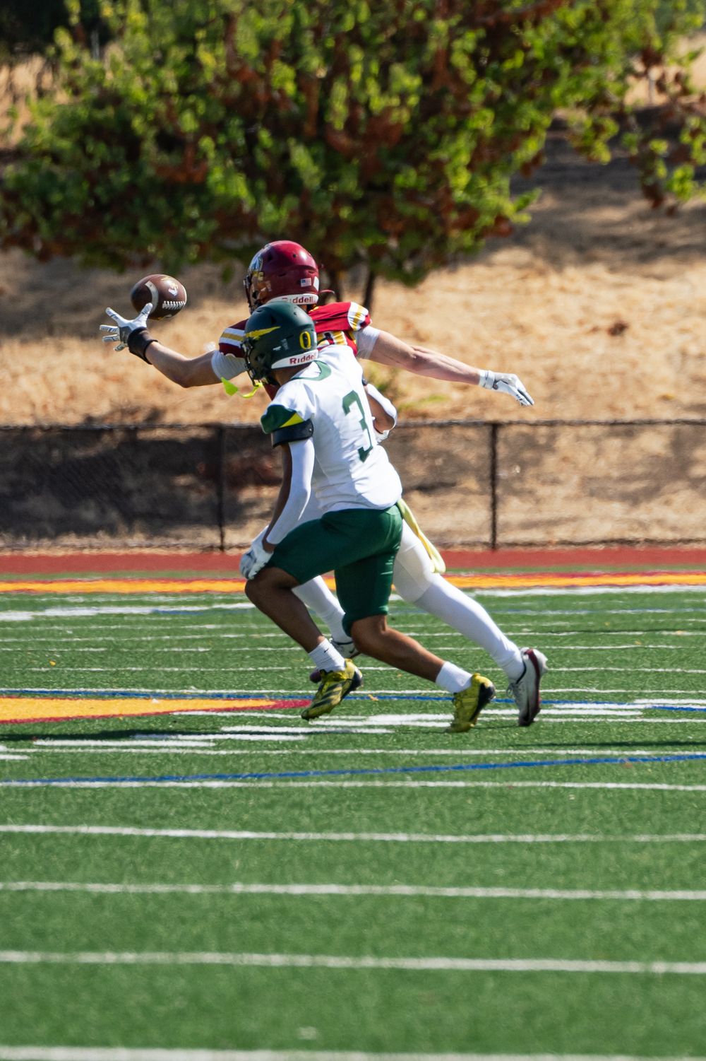 Football players in white and green uniforms collide during a tackle on the field.