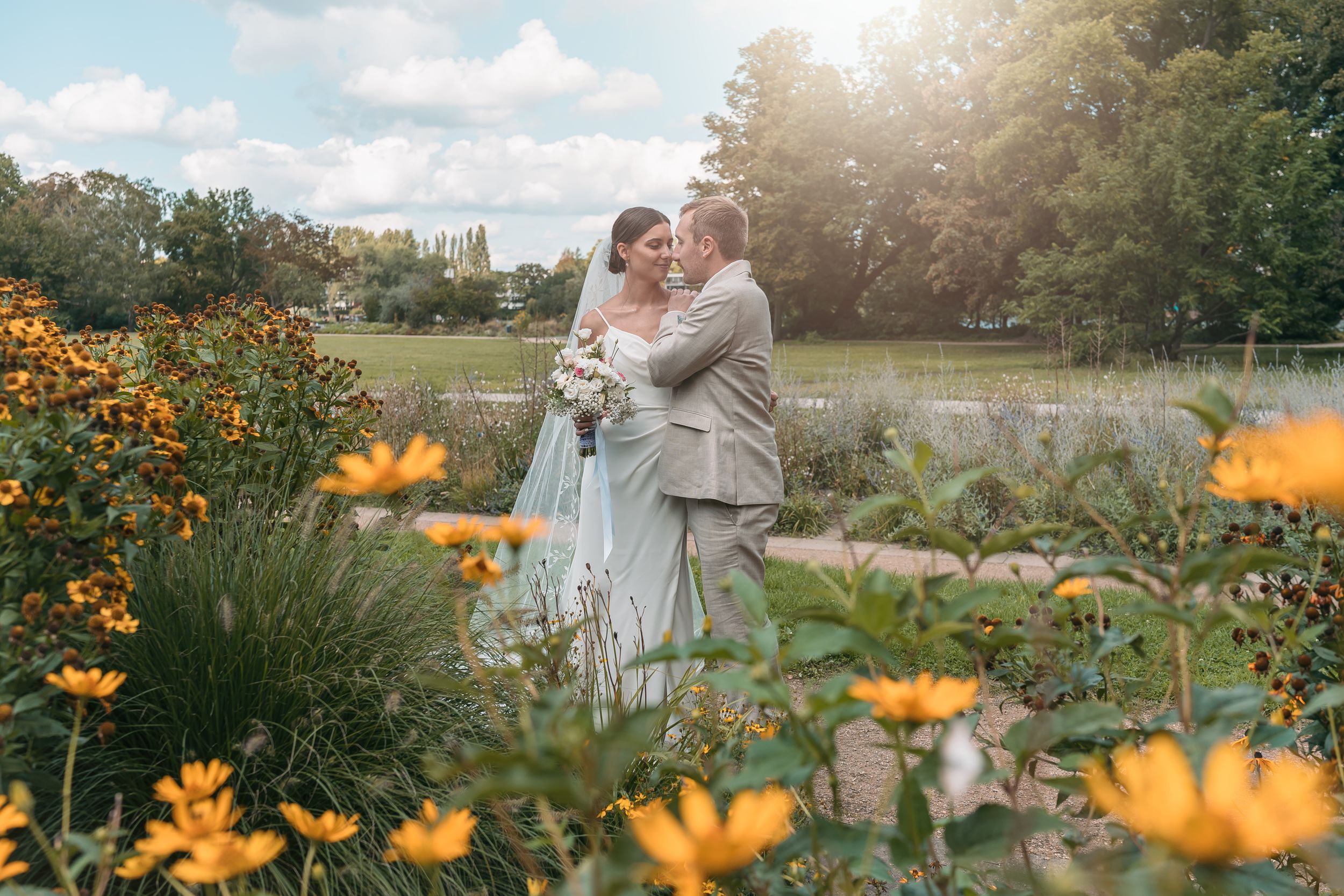 Hochzeitsfotograf in Treptow-Köpenick - Leidenschaftlicher Kuss in Park mit grünen Bäumen und blühenden Blumen.