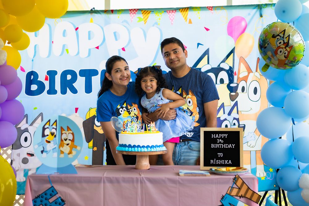 Family celebrating with Bluey themed birthday cake and balloon decorations.