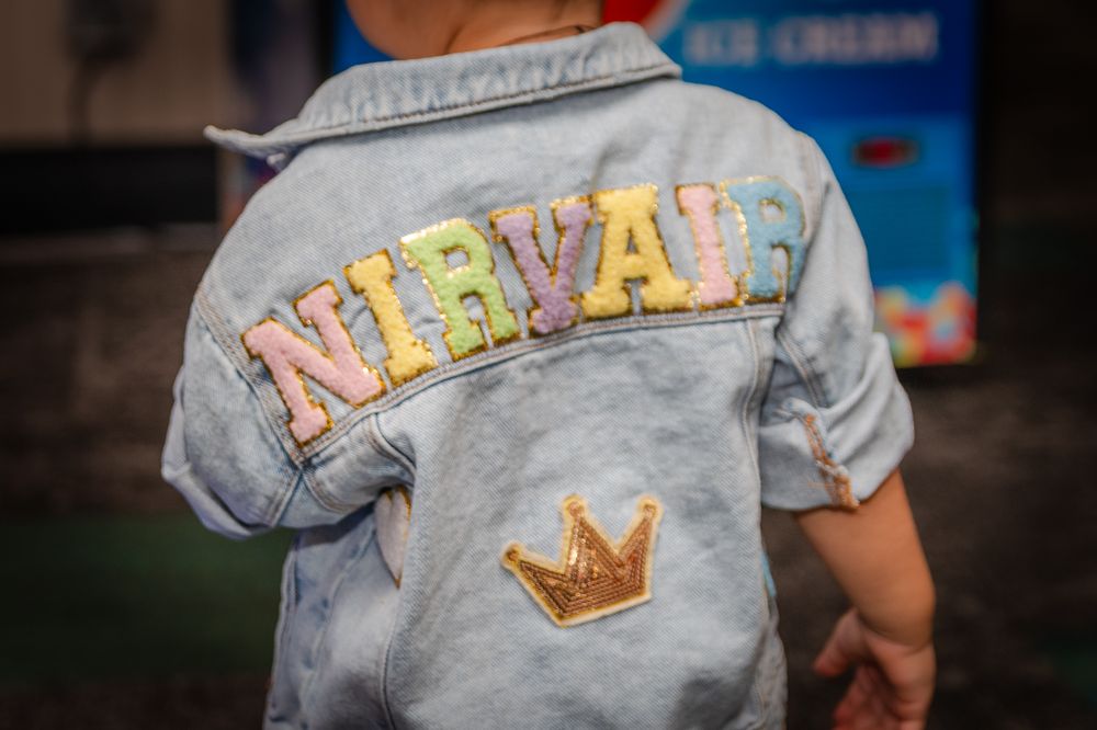 Close-up of denim jacket with colorful 'Nevada' text and crown embroidery.