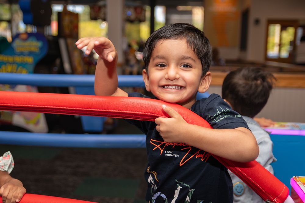 Child playing joyfully at an indoor play area with colorful equipment.