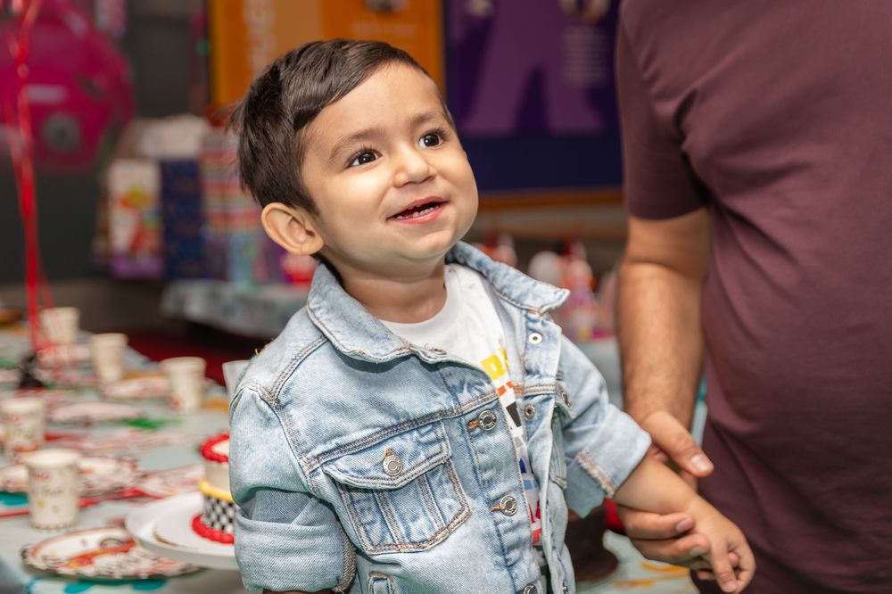Child in denim jacket smiling while playing at an indoor event.