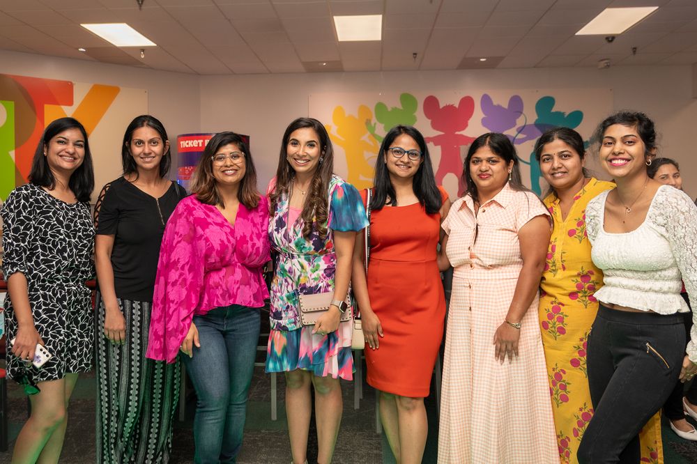 Group photo of women in colorful outfits against a rainbow backdrop.