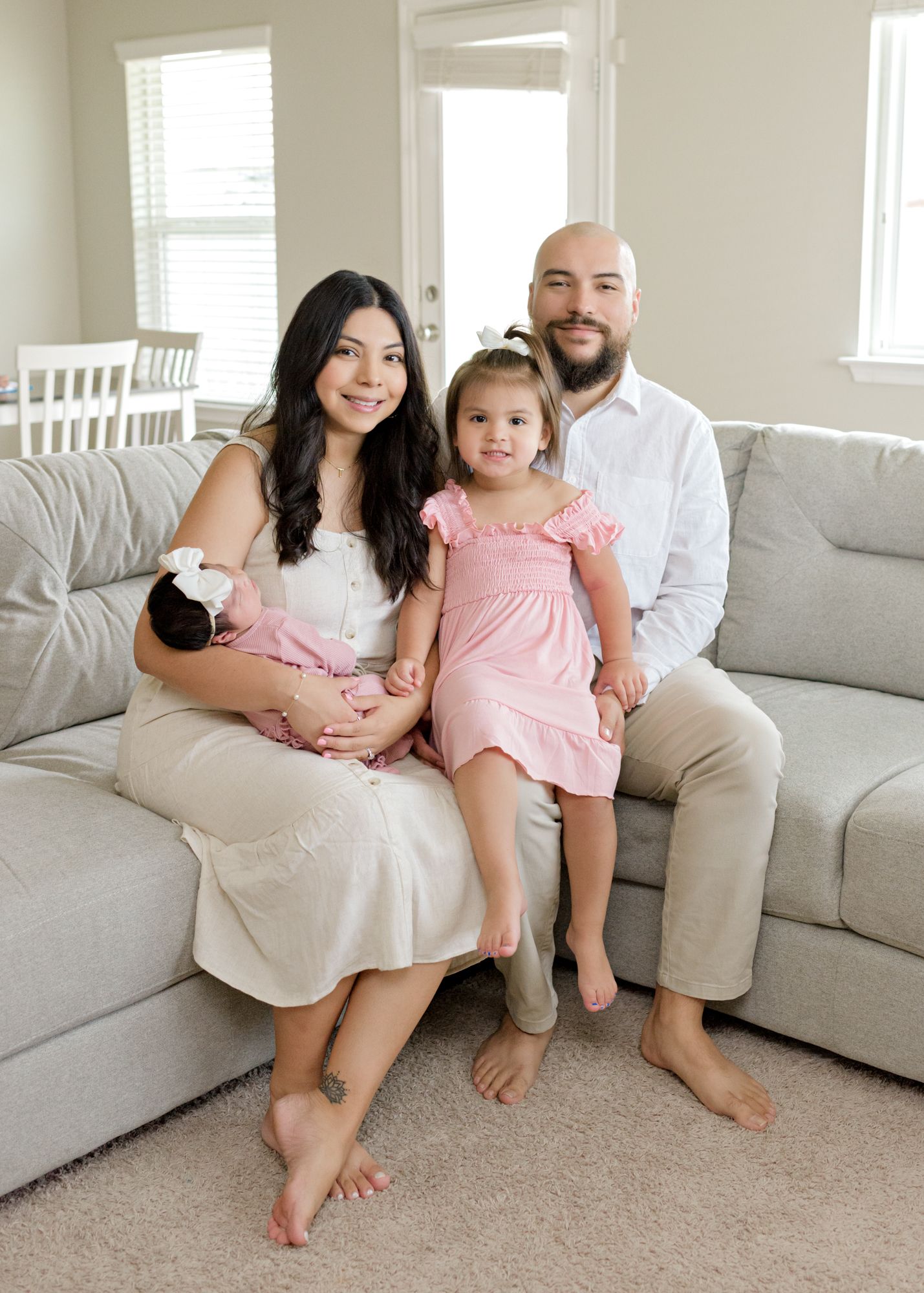 A family portrait on a couch with everyone barefoot in coordinated neutral colors.