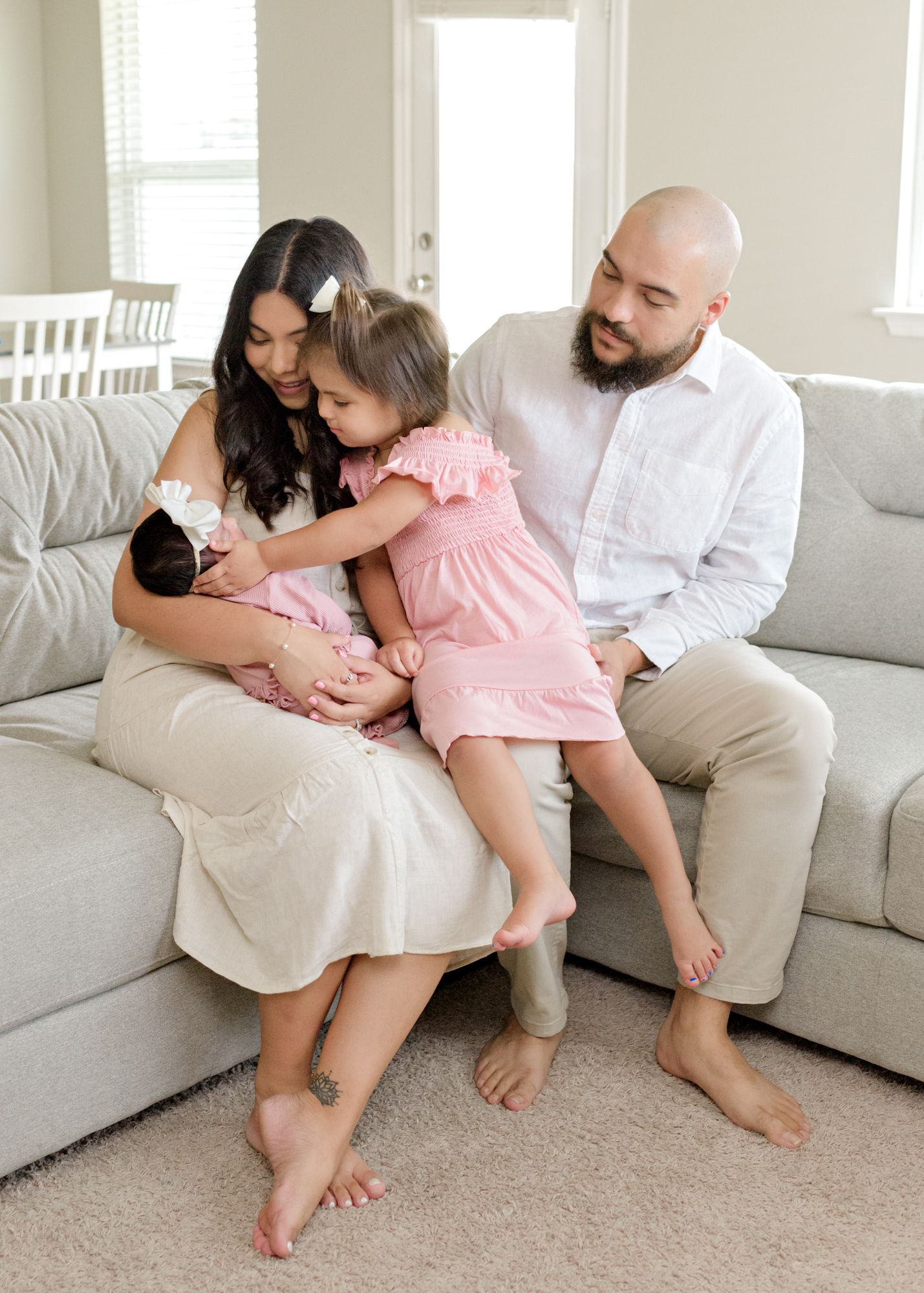 A family moment on a grey couch with a newborn baby and young child in pink.