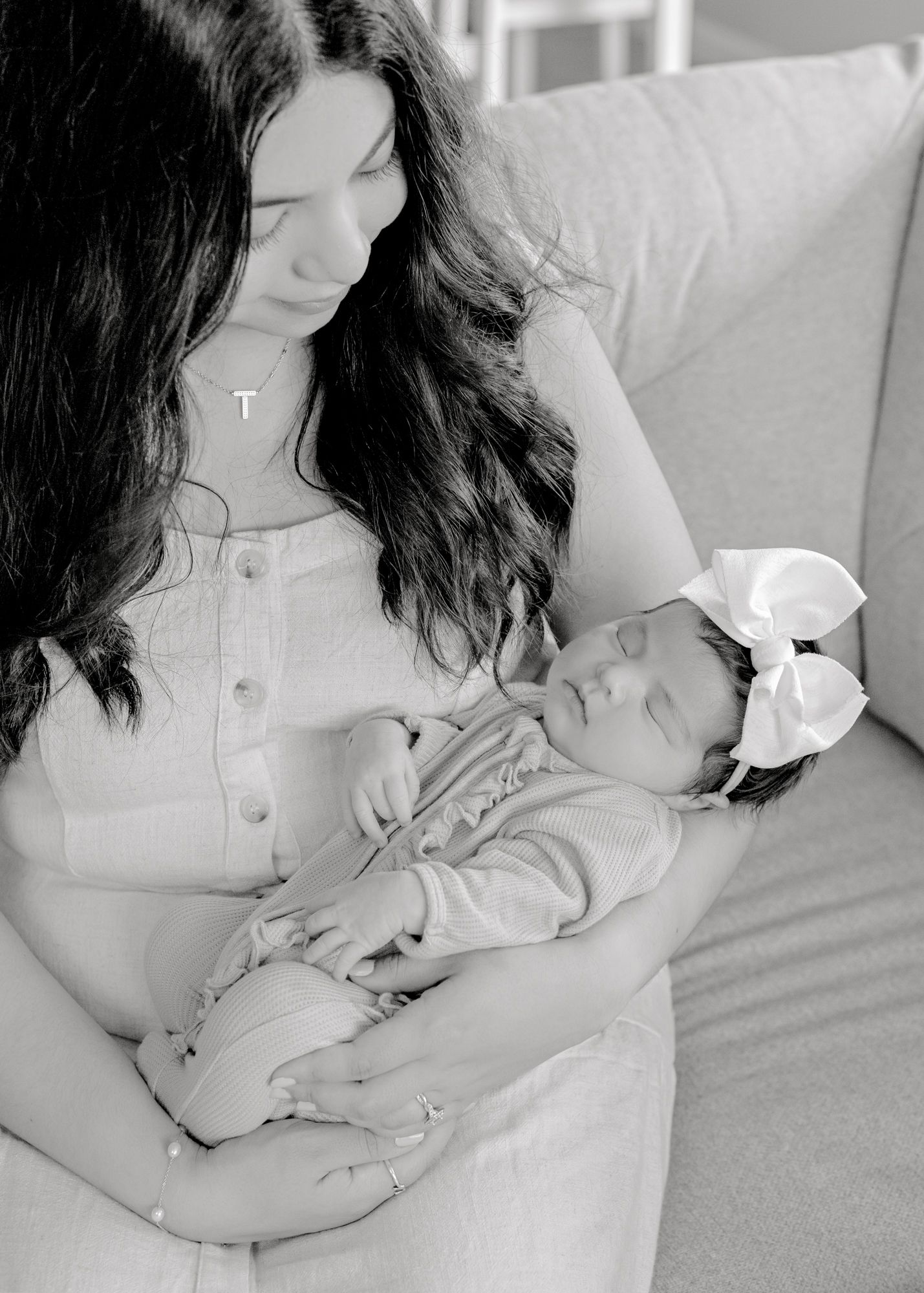 A black and white portrait of a mother holding her sleeping newborn on a couch.