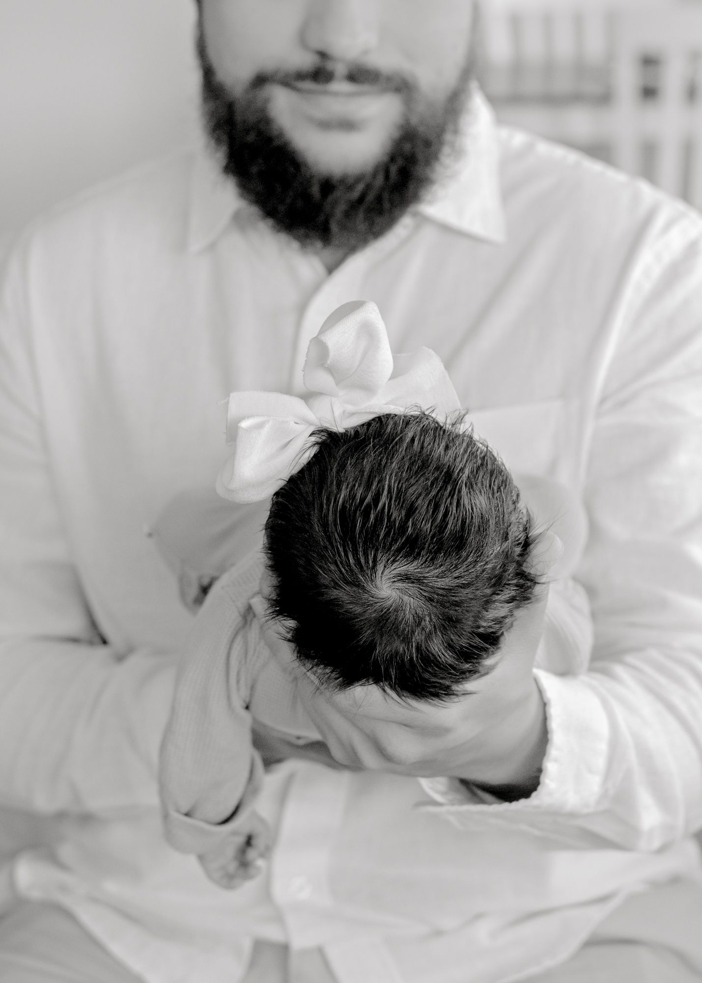 Black and white portrait showing gentle moment with an infant wearing a white bow.
