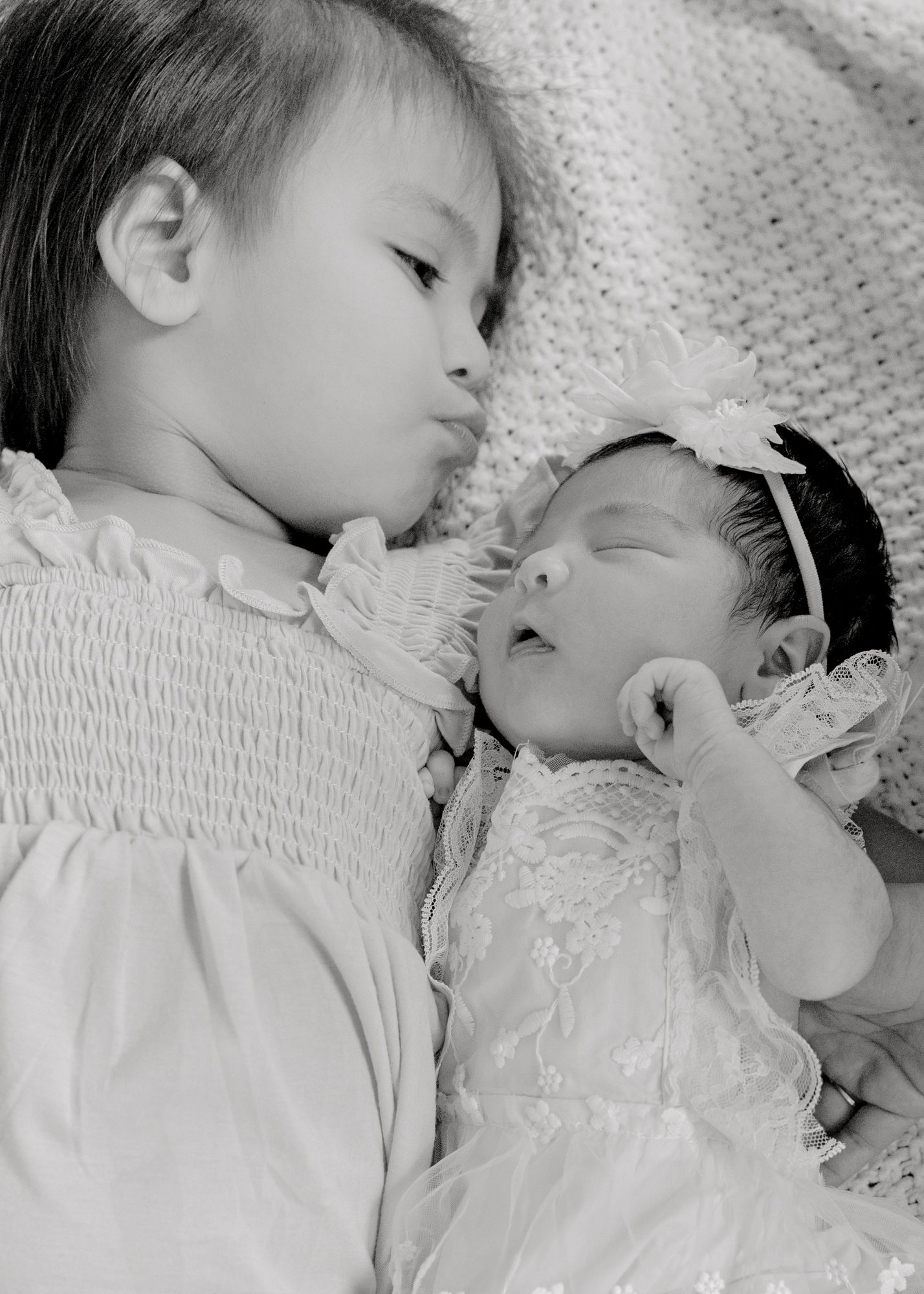 Black and white photo of siblings sleeping together on textured blanket.