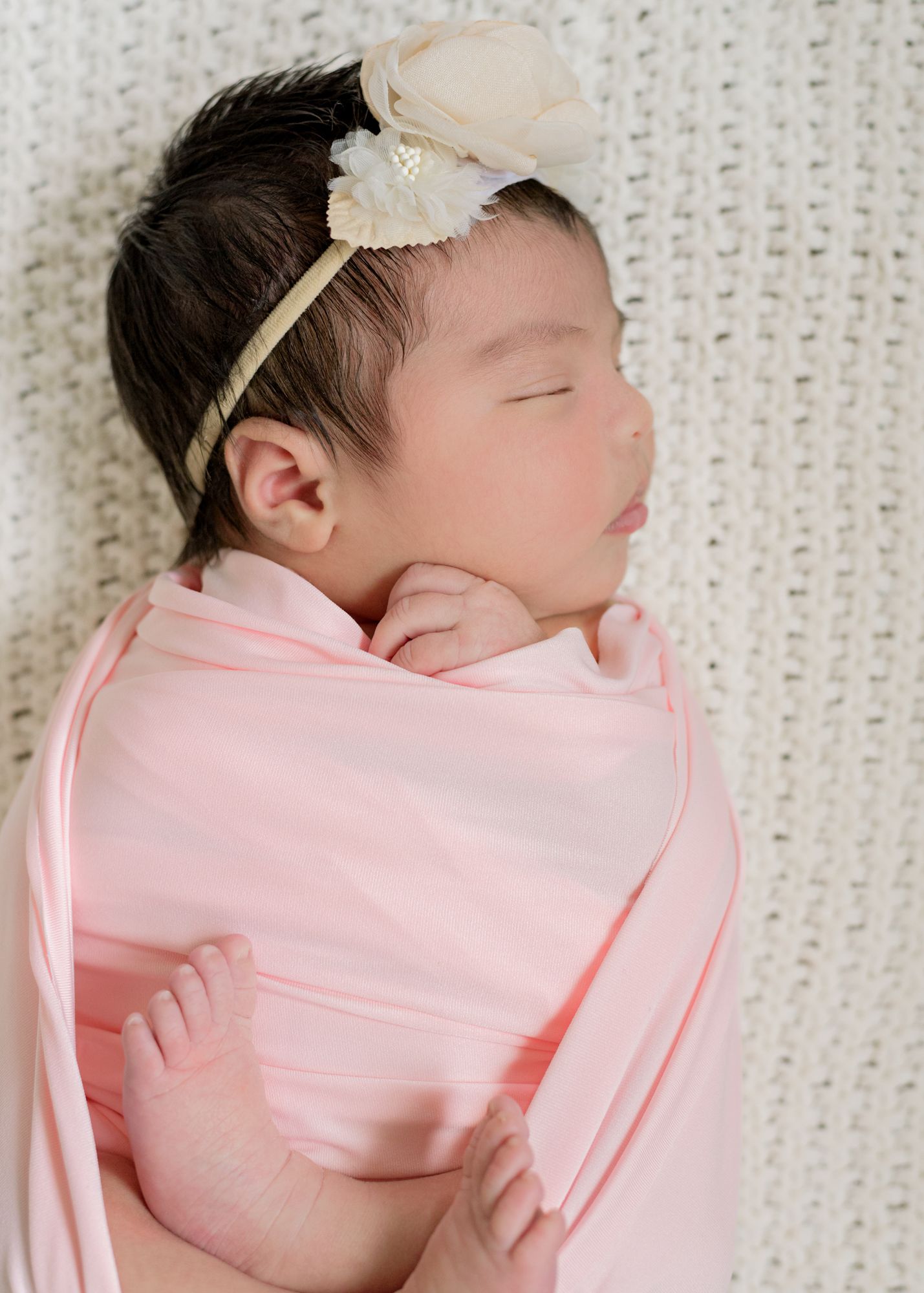 Sleeping newborn wrapped in soft pink blanket wearing floral headband.