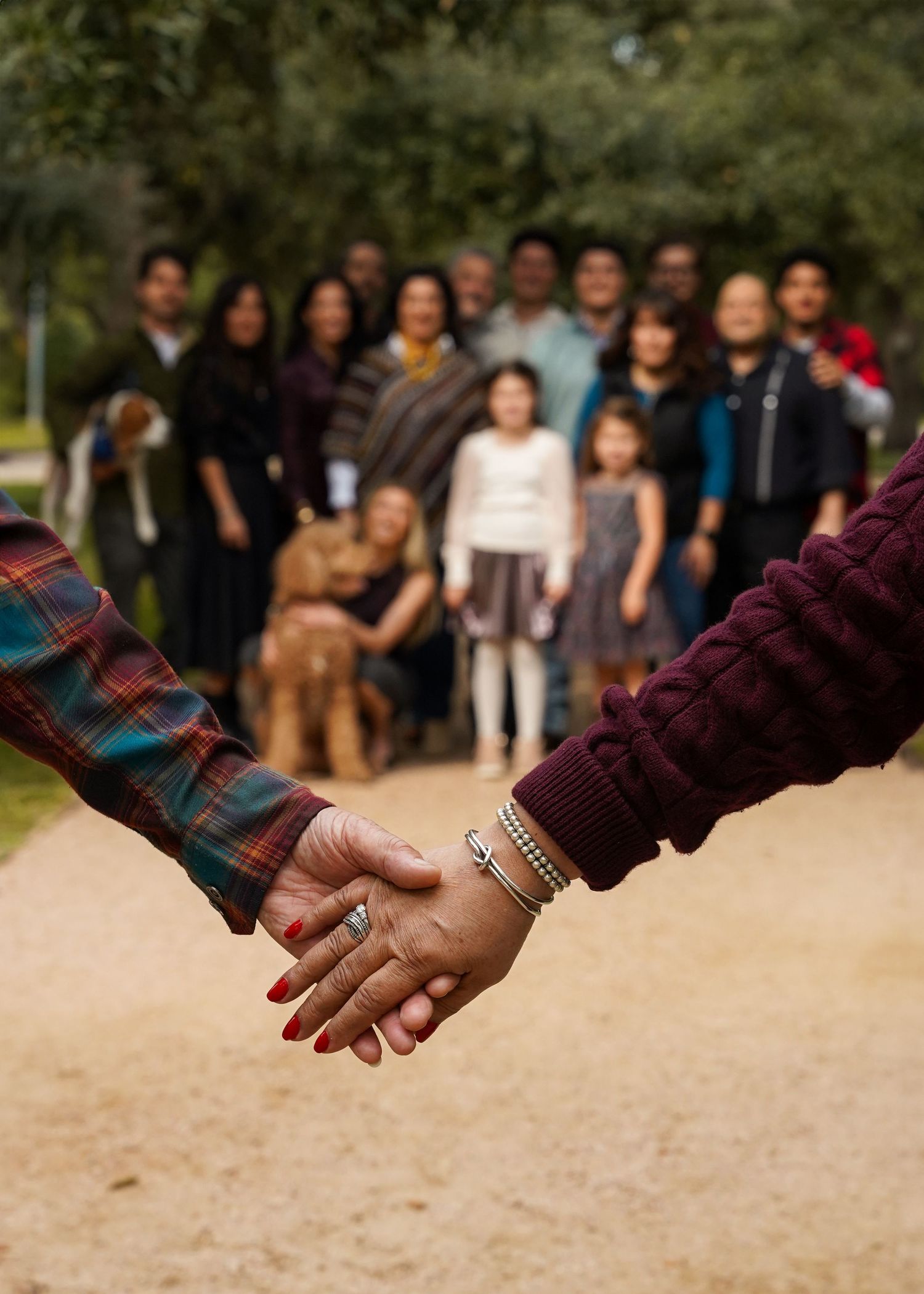 Two hands clasped together with a family gathering visible in the background.