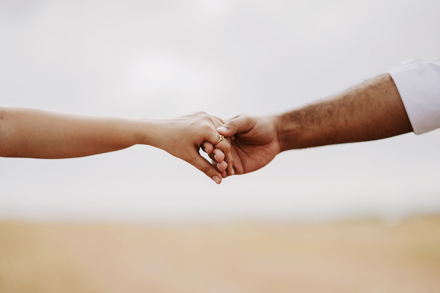 Two hands tenderly hold each other against a soft blurred outdoor background.