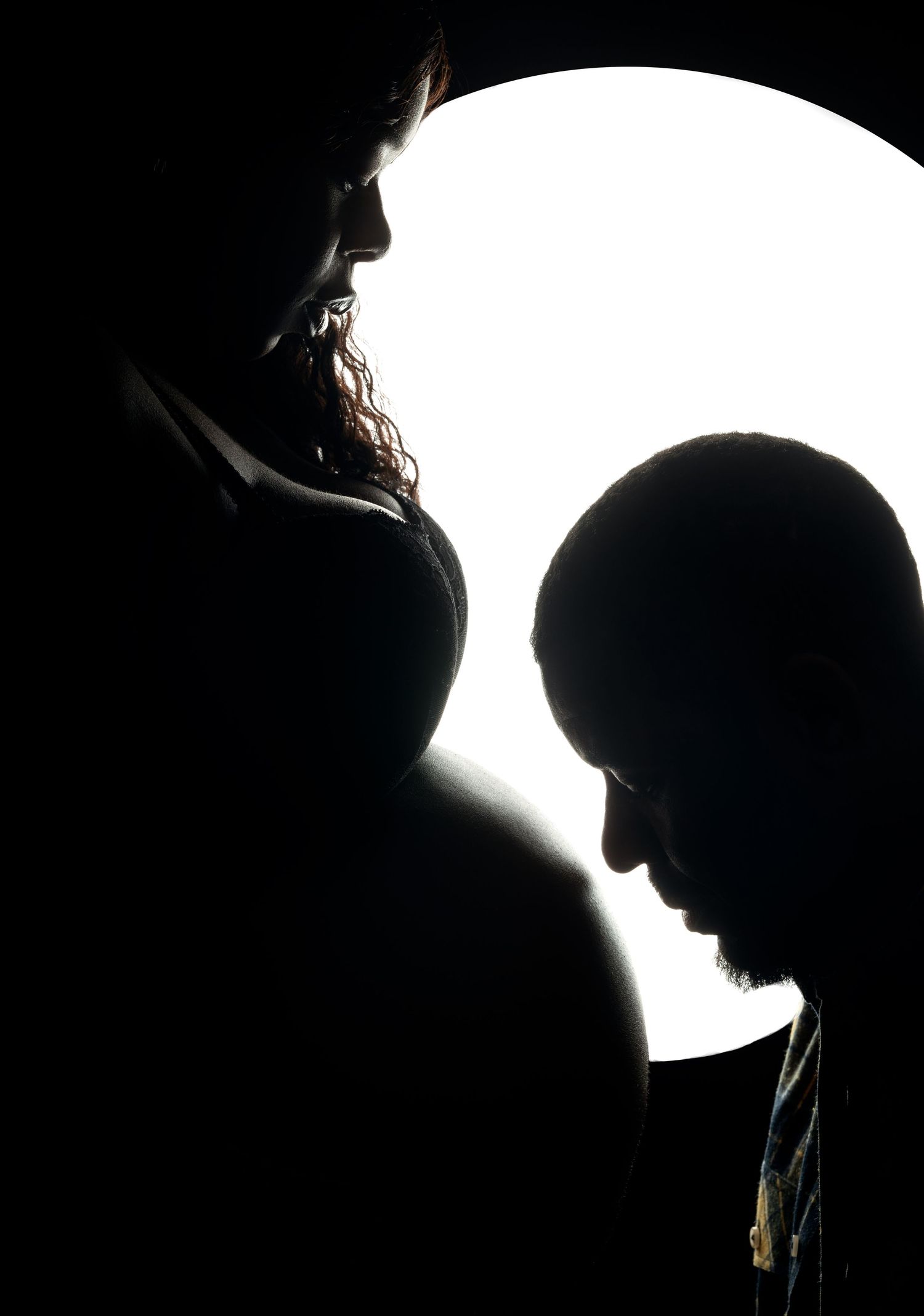 Artistic silhouette portrait of two people against bright white circular background.