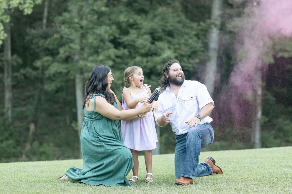 Outdoor family photography session with pink smoke effects in a green field.