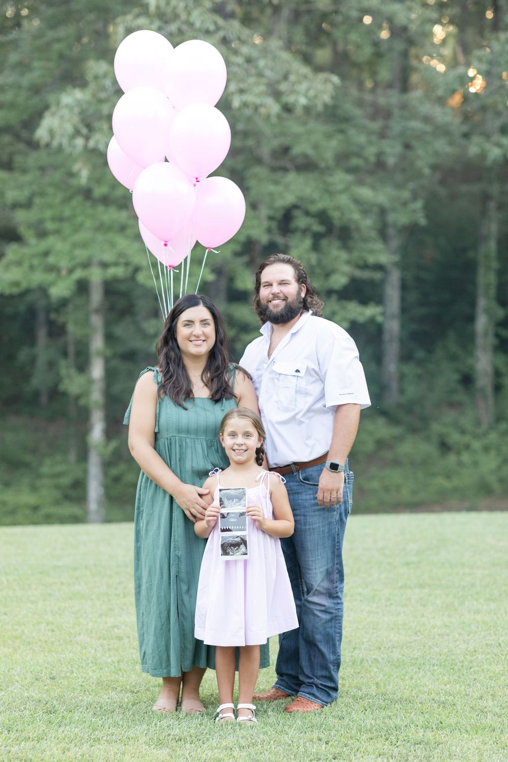 Family photoshoot in a grassy field with pink balloons and casual attire.