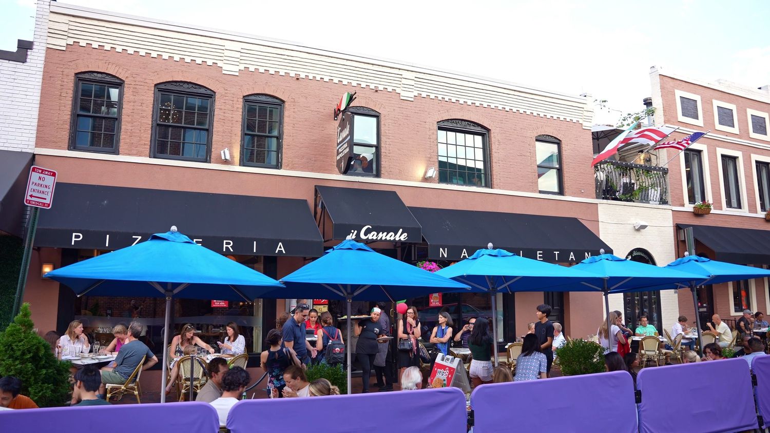 Outdoor dining area with blue umbrellas in front of a historic brick building.
