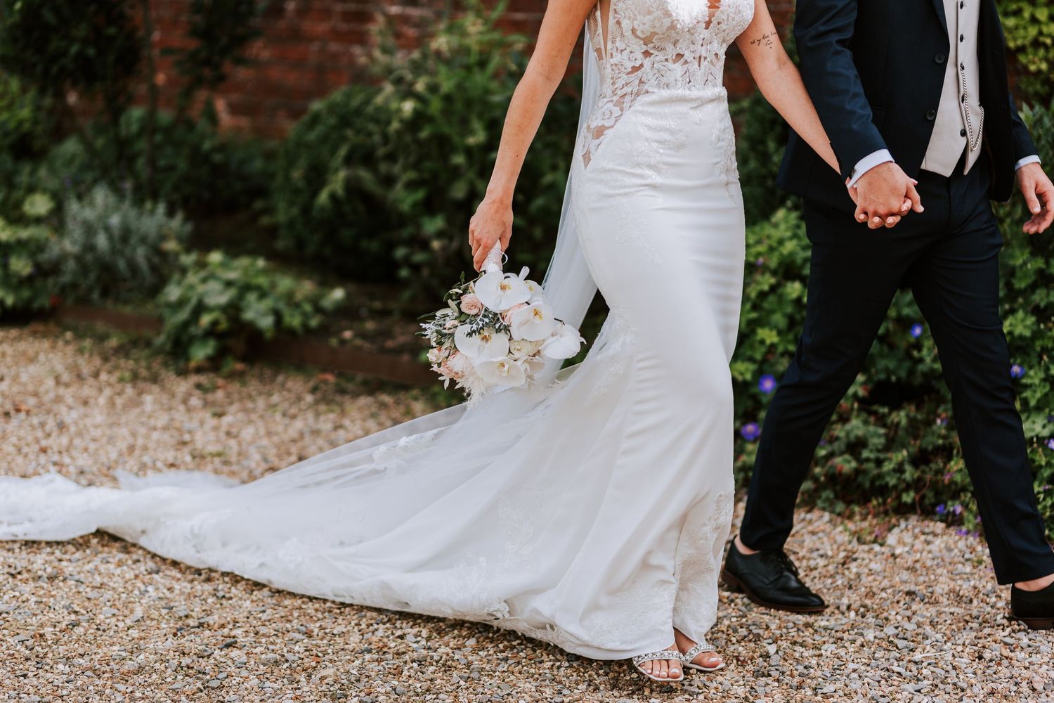 Detail shots of white wedding dress trains on gravel pathway.
