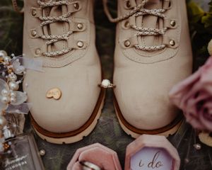 Wedding ring displayed between laces of beige combat boots with floral accents.