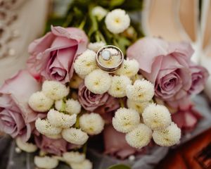 Wedding rings nestled among pink roses and white button flowers in a romantic wedding detail shot.