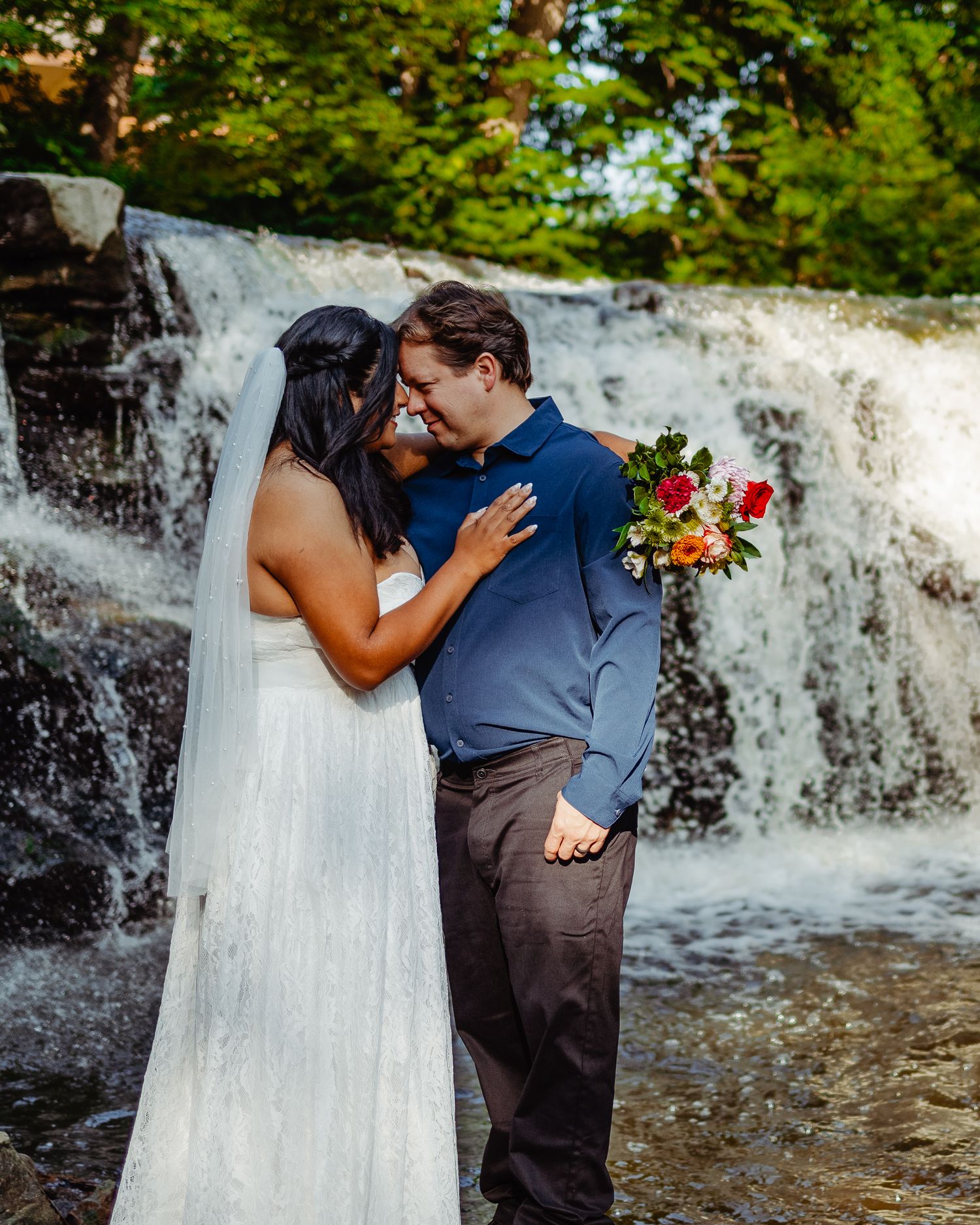 A couple shares an intimate moment by a waterfall during their wedding ceremony.