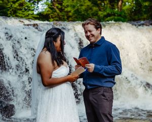 A couple shares a romantic moment by a cascading waterfall while exchanging rings during an intimate ceremony.
