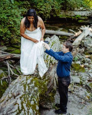 A heartwarming wedding moment captured on natural rock formations by a flowing stream.