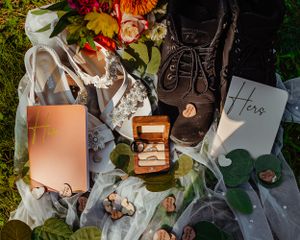 Wedding details flatlay featuring brown boots, rings, and floral arrangements on white fabric.