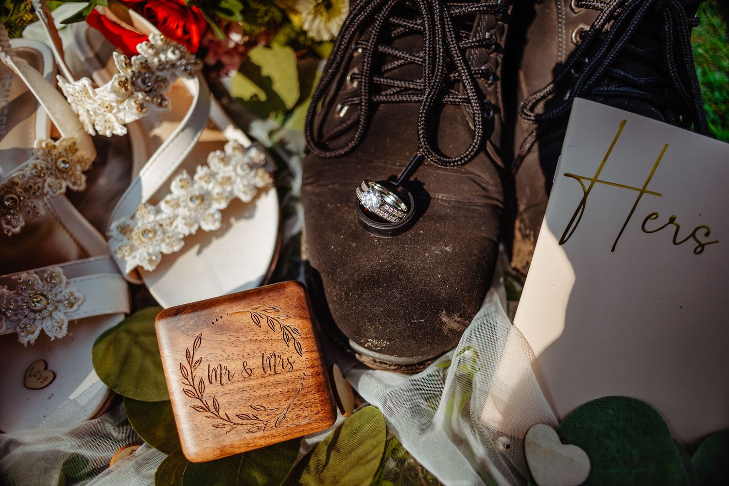 Wedding detail shot of rings, boots and cards arranged artistically with greenery.