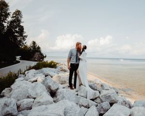 A sunset wedding portrait captured on white coastal rocks overlooking a serene waterfront.