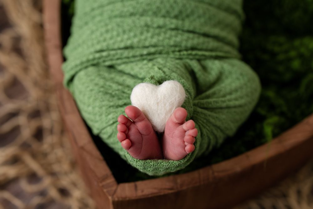 baby toes sticking out of a green swaddle with a felt heart in between