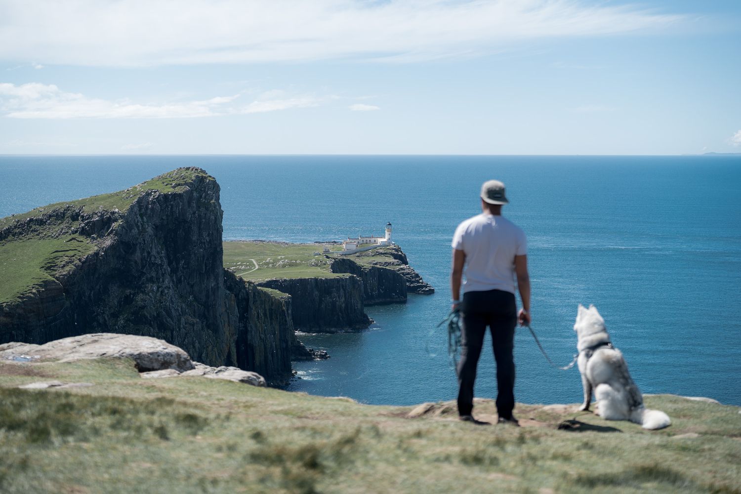 randonneur et son chien devant les falaises de neist point et le phare sur l'île de skye en ecosse