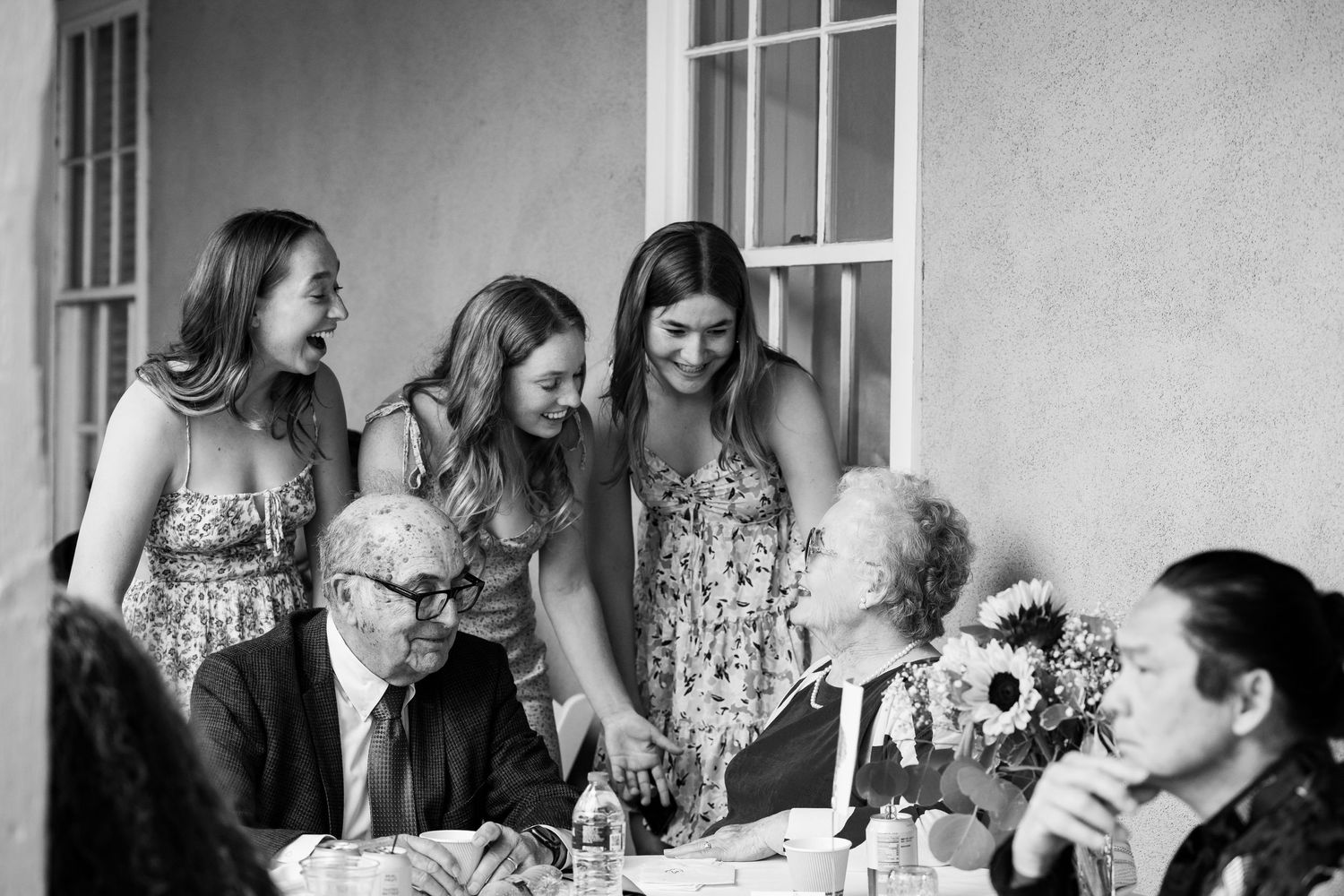 A black and white photo captures a multi-generational gathering around a table with sunflowers.