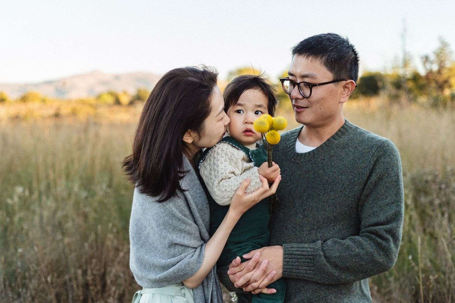 Family sharing a tender outdoor moment in autumn fields during golden hour.
