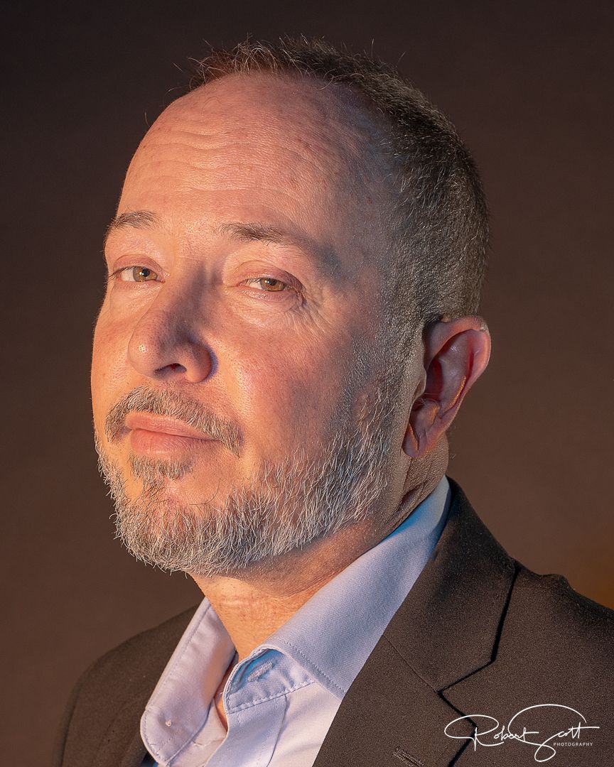 Studio portrait of man in business attire with beard against dark backdrop.