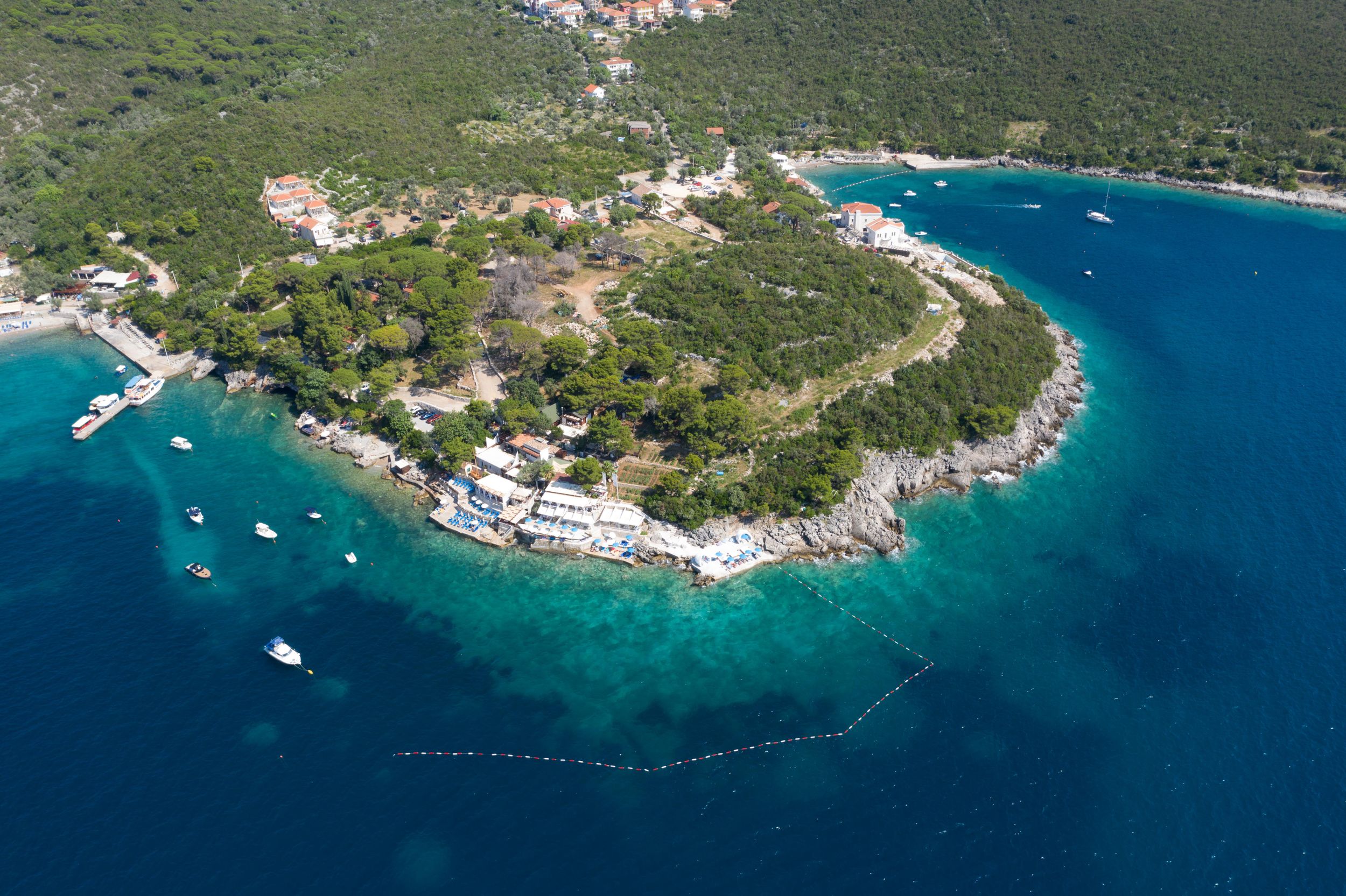 Aerial view of a Mediterranean coastline with turquoise waters, boats, and a small developed peninsula.