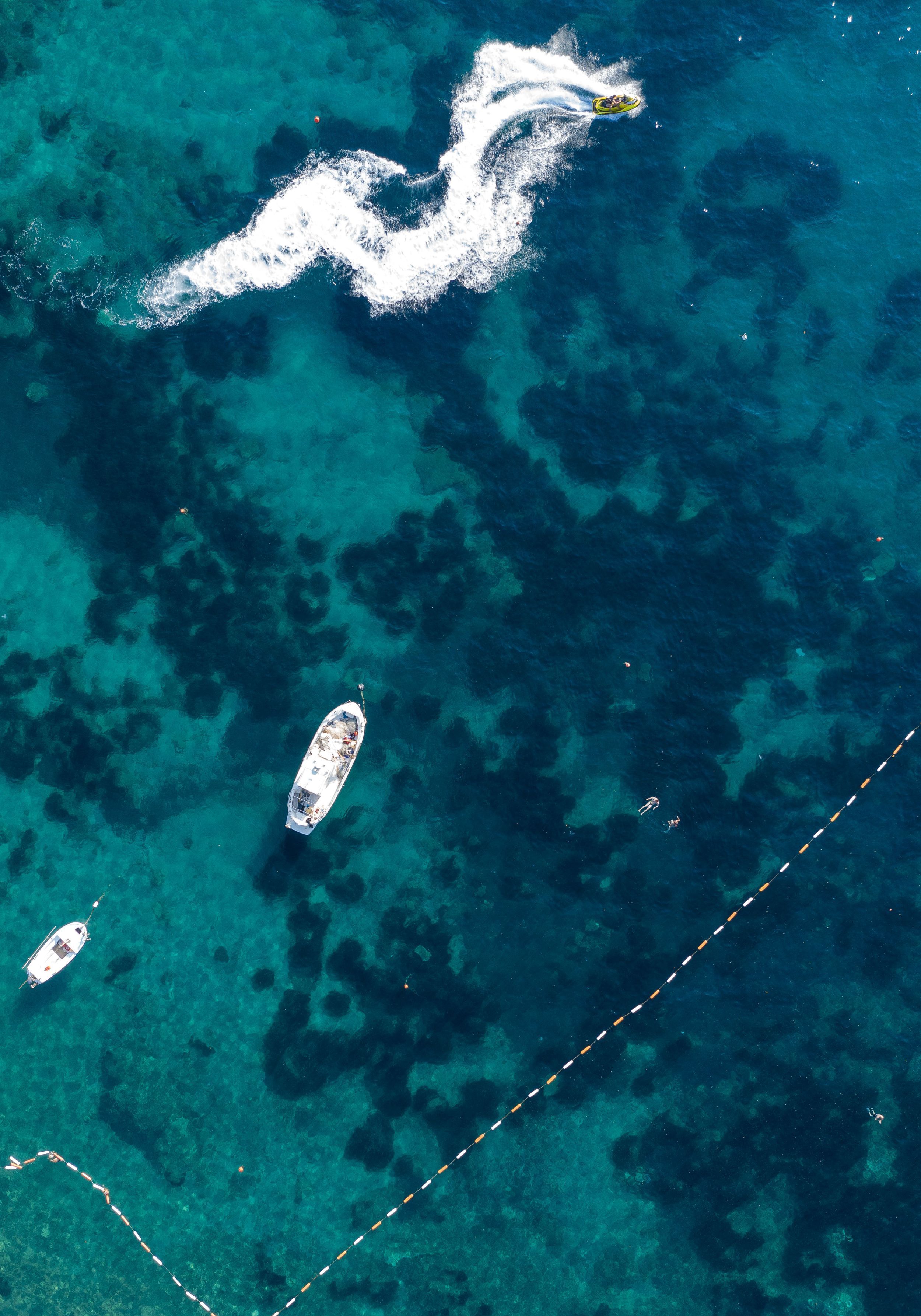 Aerial view of boats in crystal clear turquoise water with white wake patterns.