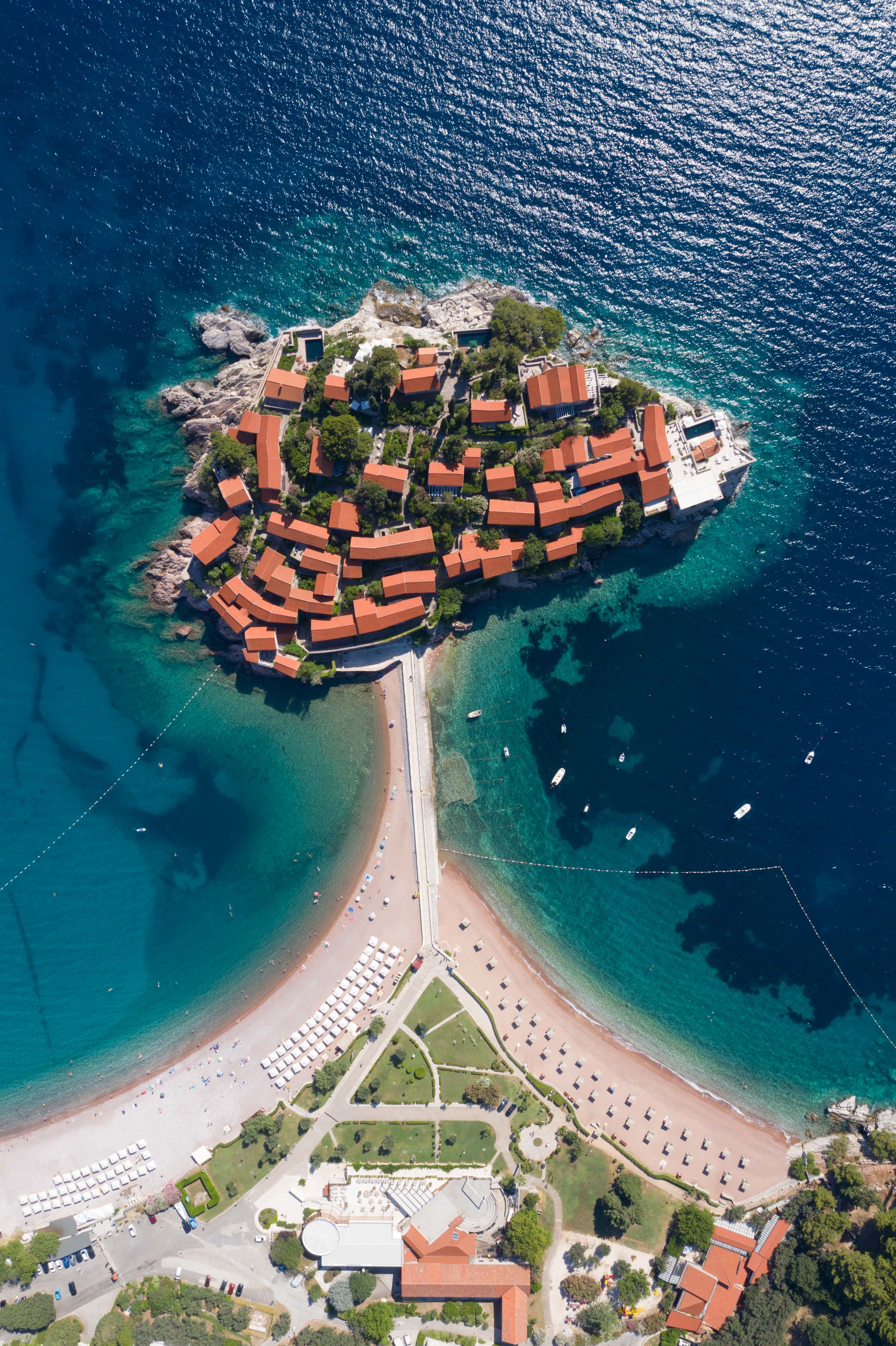 Aerial view of Sveti Stefan island resort in Montenegro connected to mainland by a narrow sandy beach.
