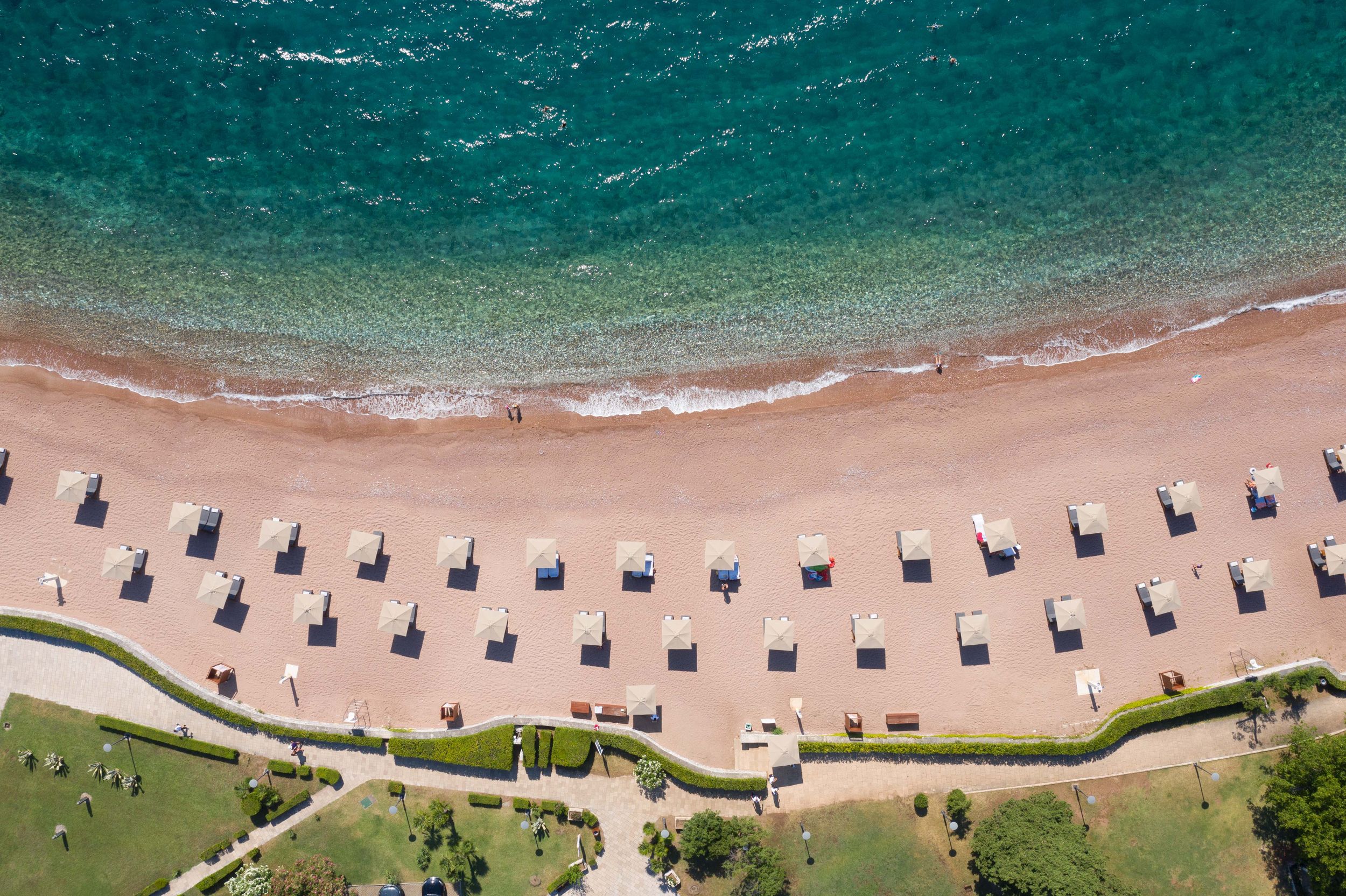 Aerial view of perfectly aligned beach umbrellas creating patterns along turquoise shoreline.