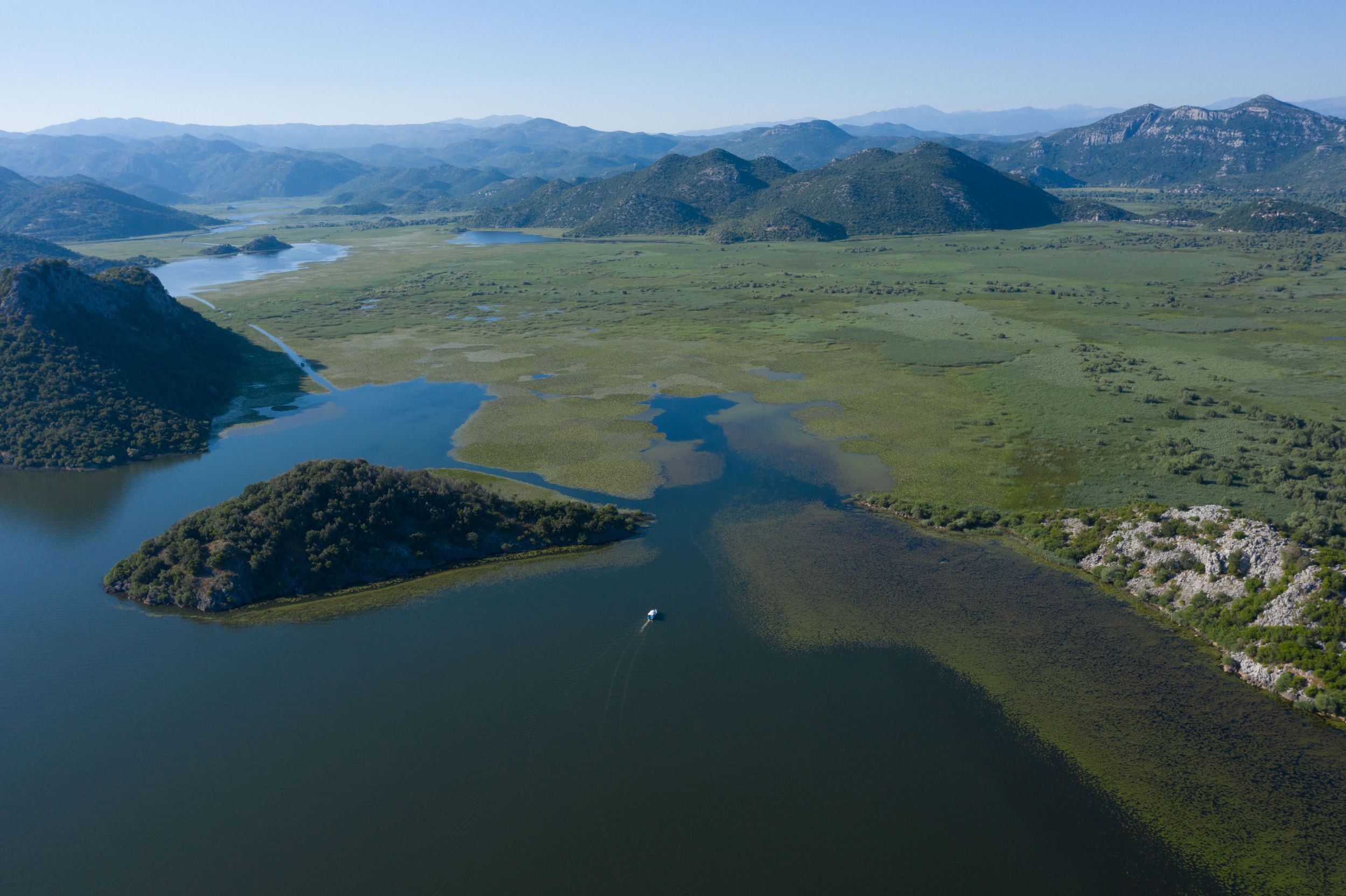 Aerial view of a vast green landscape with winding waterways and mountains in the distance.