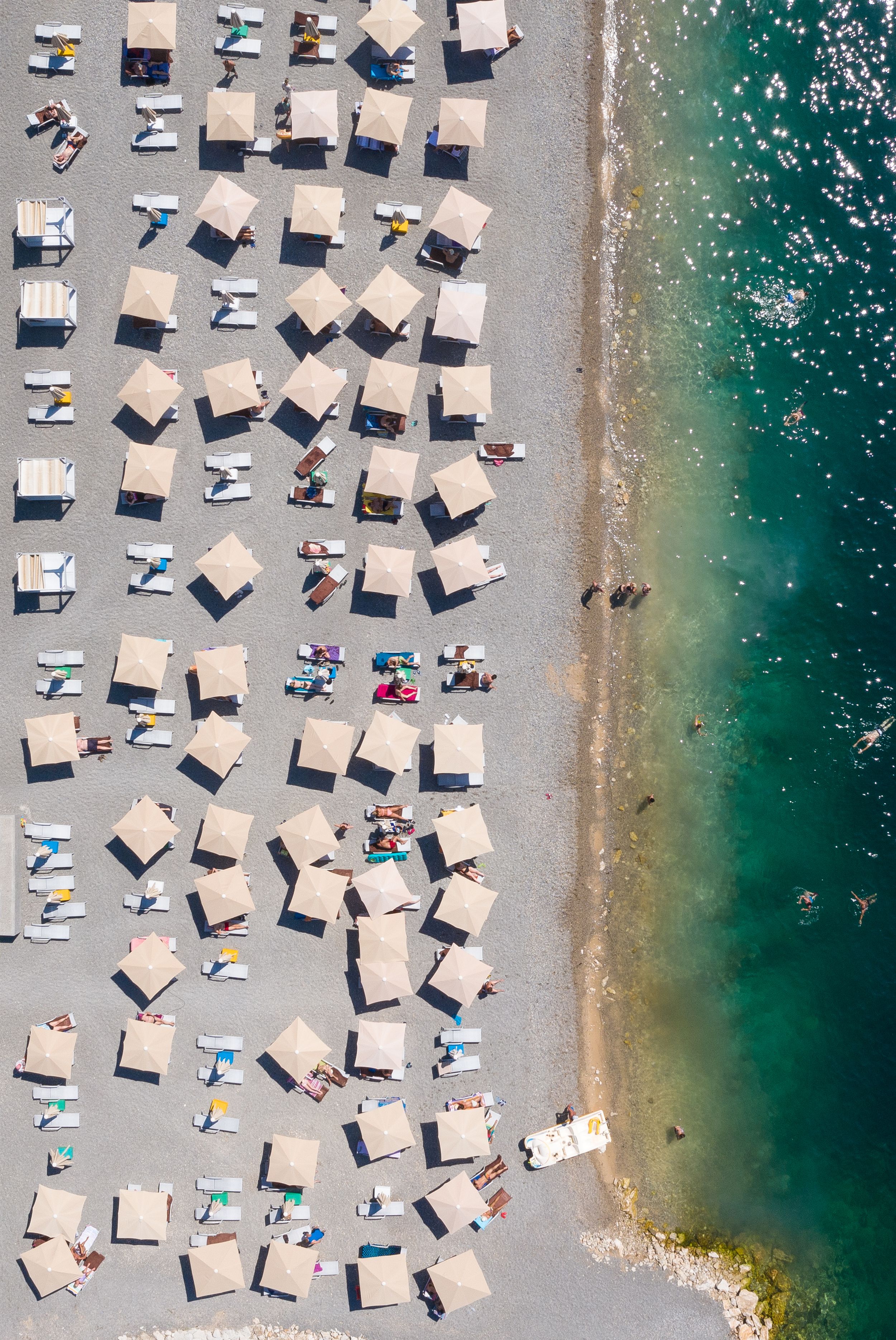 Bird's eye view of neatly arranged white beach cabanas along turquoise coastline.