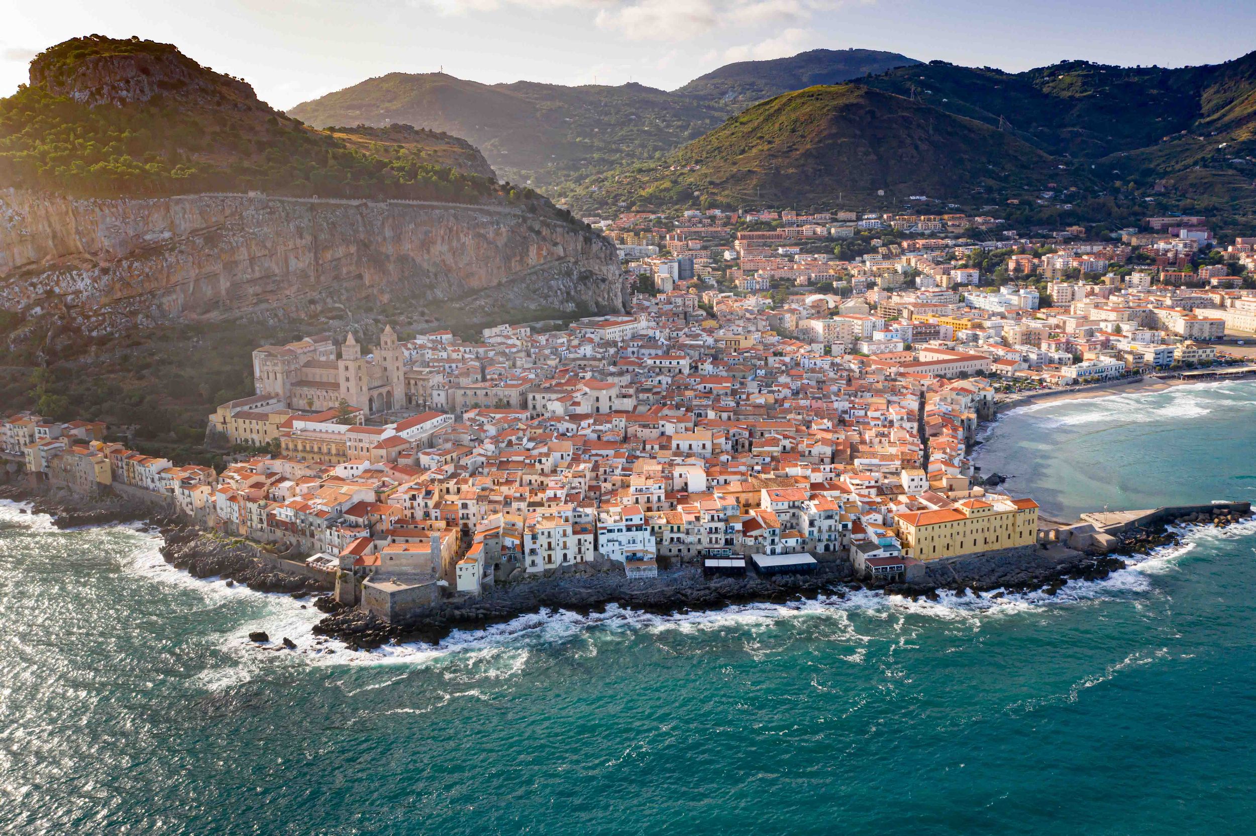 Aerial view of a coastal Mediterranean town nestled between mountains and turquoise waters.