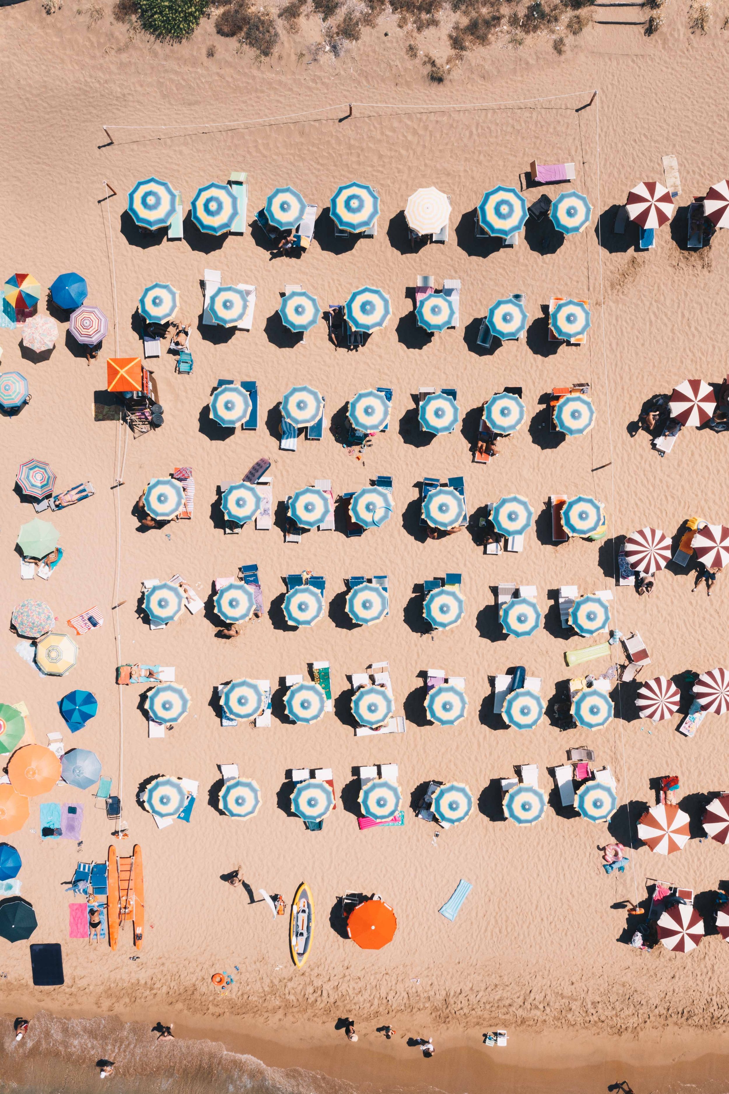 Birds-eye view of neatly arranged blue and white beach umbrellas on sandy beach.