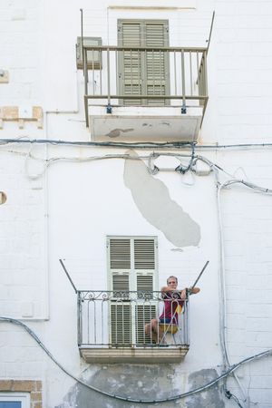 Traditional Italian balcony with green shutters on a white building with peeling paint.