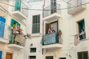 White Mediterranean buildings with colorful balconies and green shutters in an Italian neighborhood.