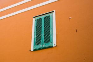 Orange building wall with single turquoise window shutters in Mediterranean style.