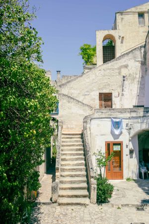 White stone building with exterior staircase and green foliage in a traditional Mediterranean style.